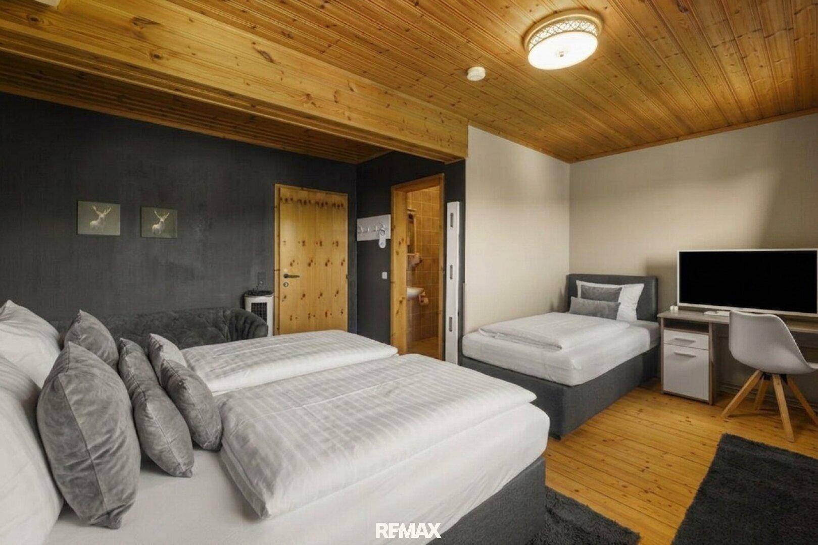 Helles Schlafzimmer mit Holzdecke, Doppel- und Einzelbett sowie einem Arbeitsbereich.