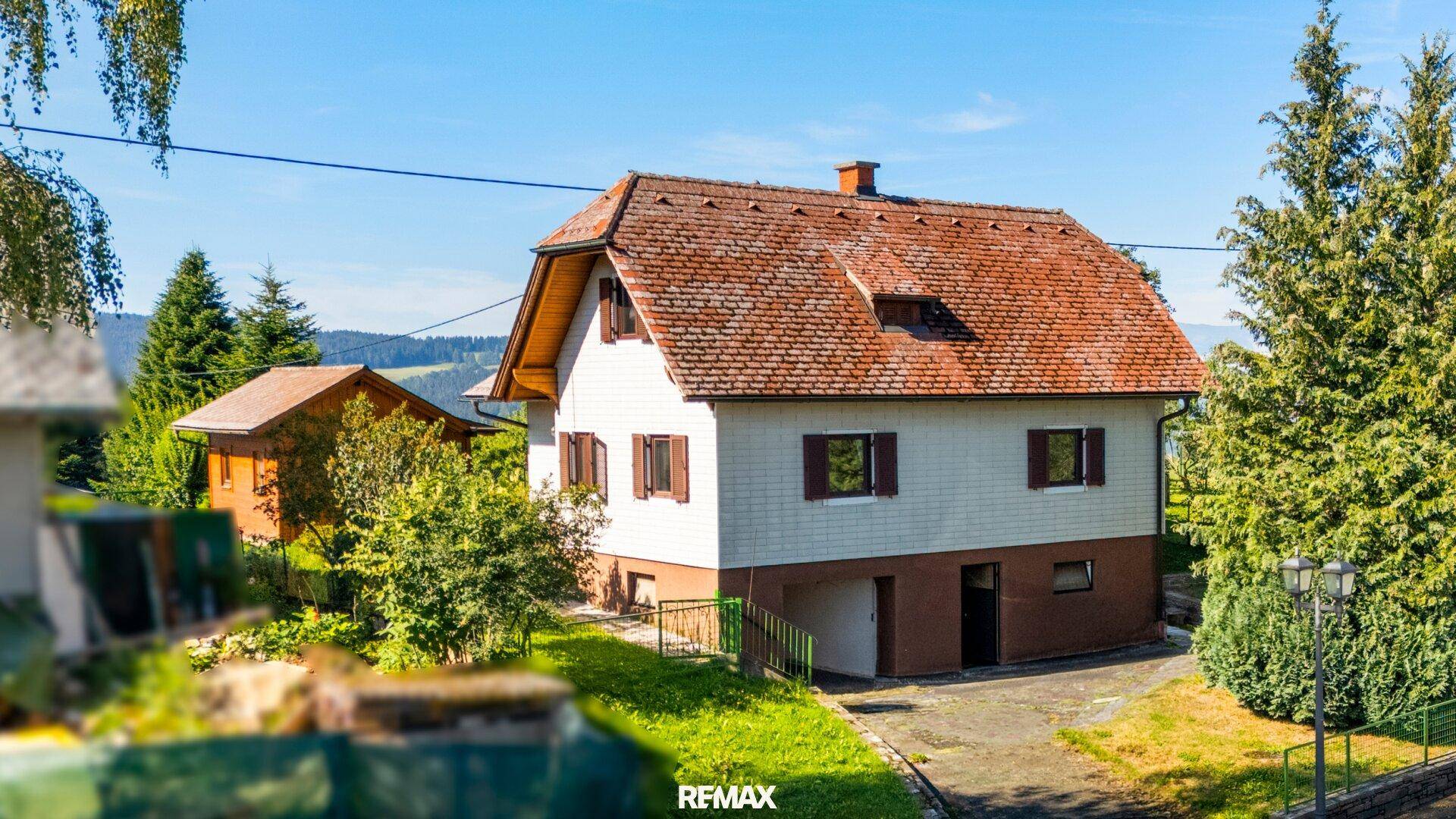 Haus mit rotem Ziegeldach, braunen Fensterläden und grüner Umgebung.