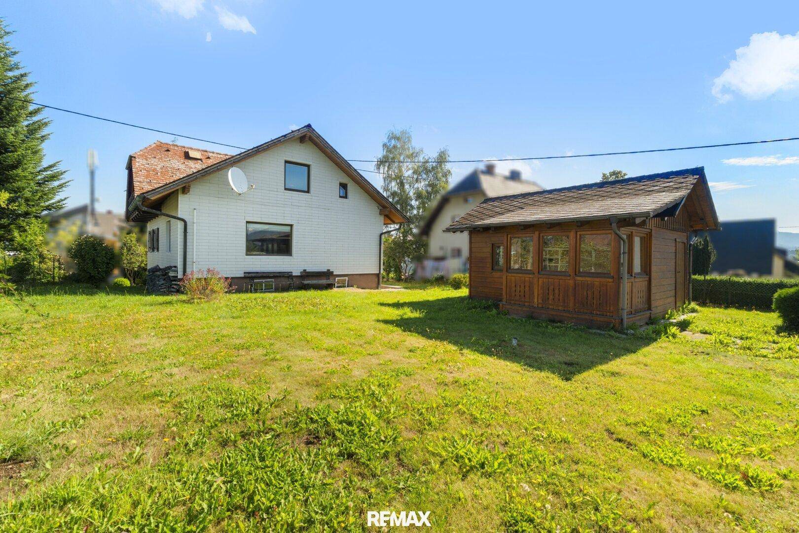 Großer Gartenbereich mit Rasenfläche und einem kleinen Holzschuppen neben dem Haus.