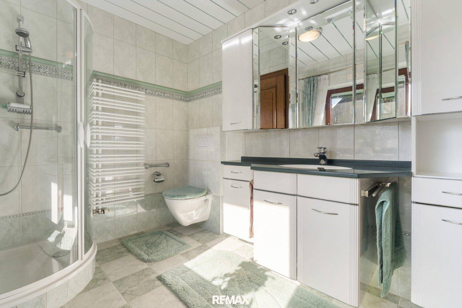 Gefliestes Badezimmer mit Dusche, Waschtisch und Spiegelschrank.
