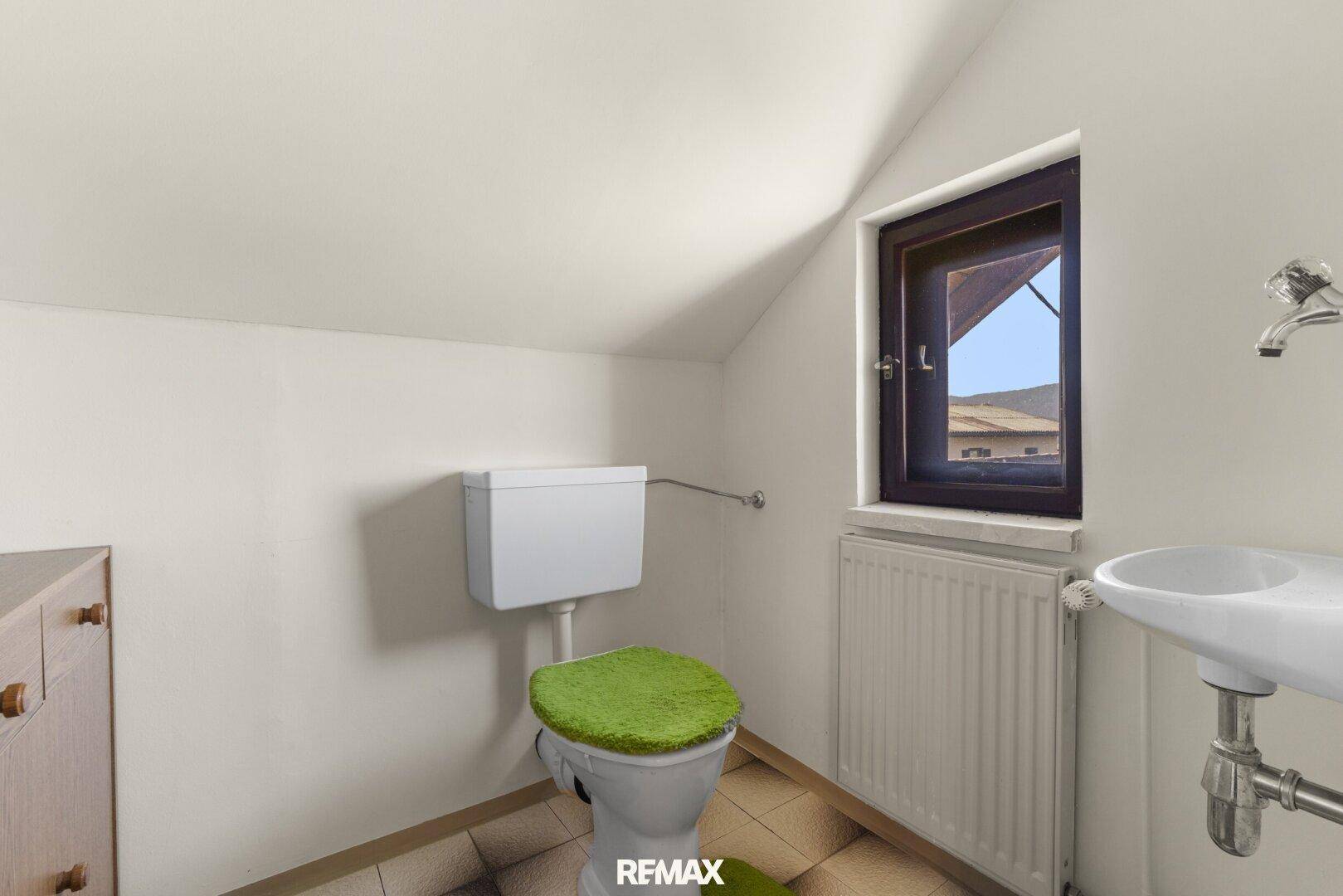 Einfaches WC im Dachgeschoss mit Fenster und schräger Decke.