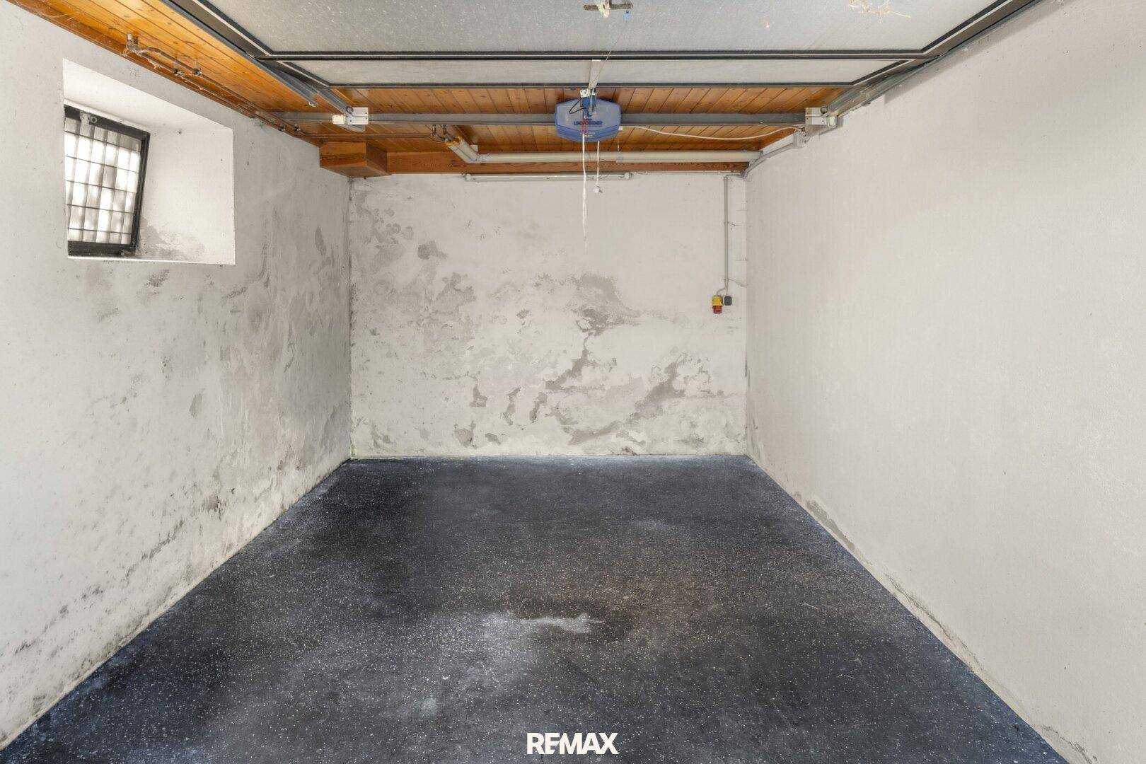 Leere Garage mit Betonboden, Fenster und einfacher Beleuchtung.