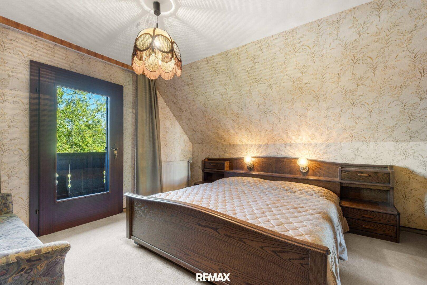 Schlafzimmer im Dachgeschoss mit Doppelbett, gemusterter Tapete und Balkonzugang.