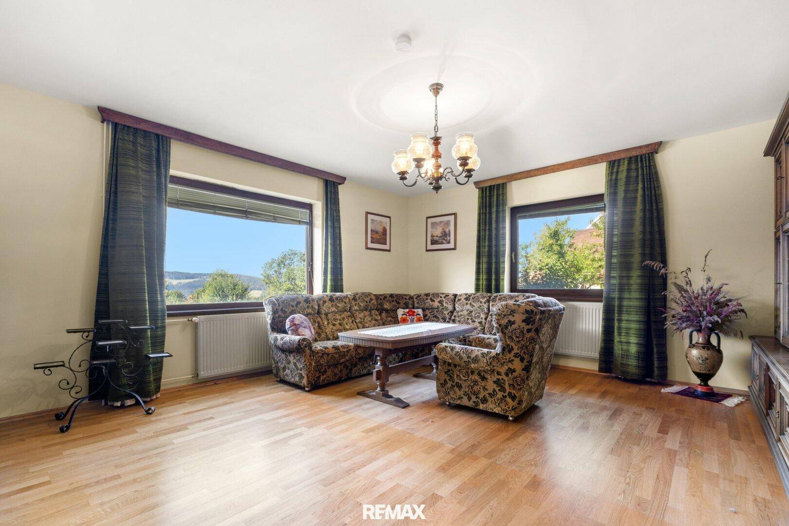 Geräumiges Wohnzimmer mit Laminatboden, großen Fenstern und Blick in die Landschaft.