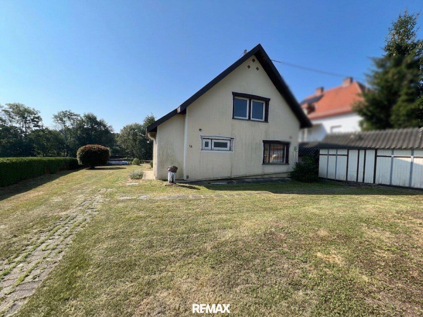 Seitenansicht des Hauses mit weitläufigem Rasen und einem kleinen Nebengebäude im Grünen.