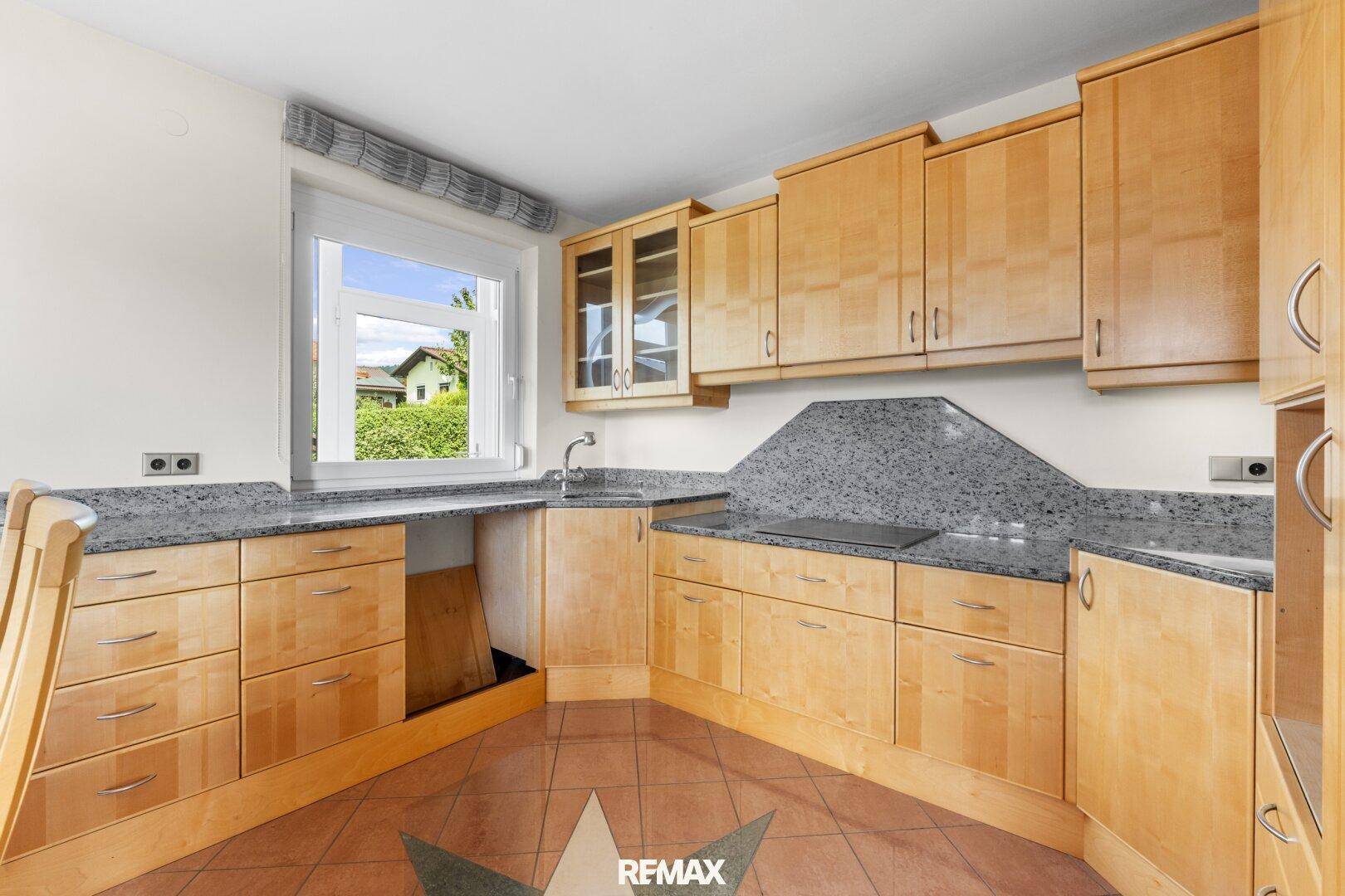 Funktionale Küche mit hellen Holzschränken, Granitarbeitsplatte und Fenster mit Grünblick.