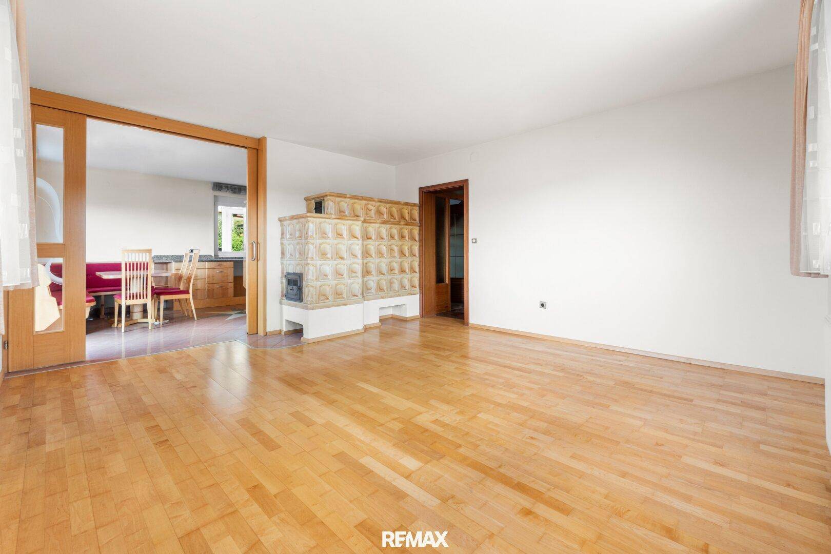 Helles Wohnzimmer mit Parkettboden und traditionellem Kachelofen, angrenzend an die Küche.