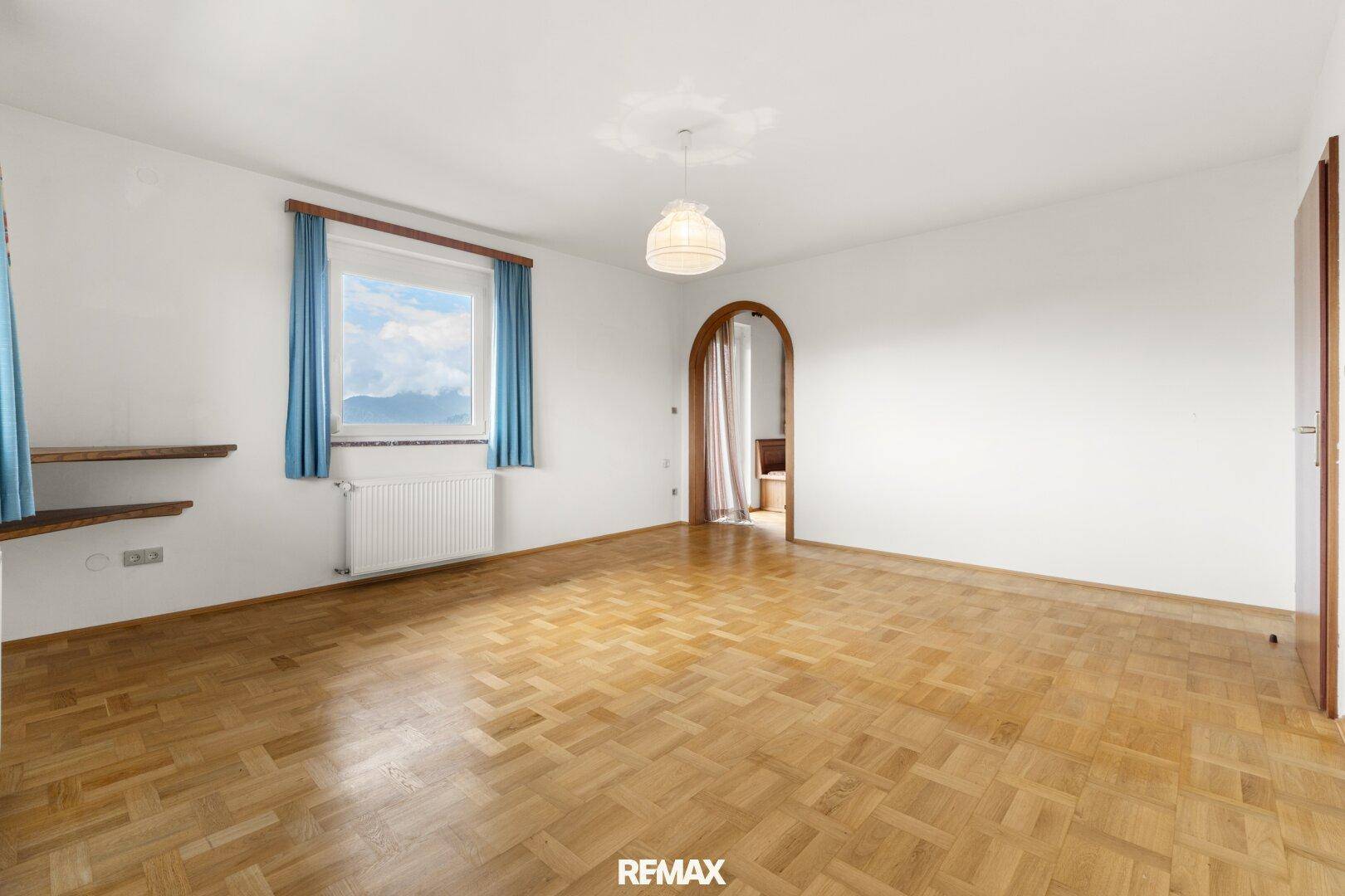 Geräumiges Zimmer mit Parkettboden und Fenster, das einen Blick auf die Berge bietet.