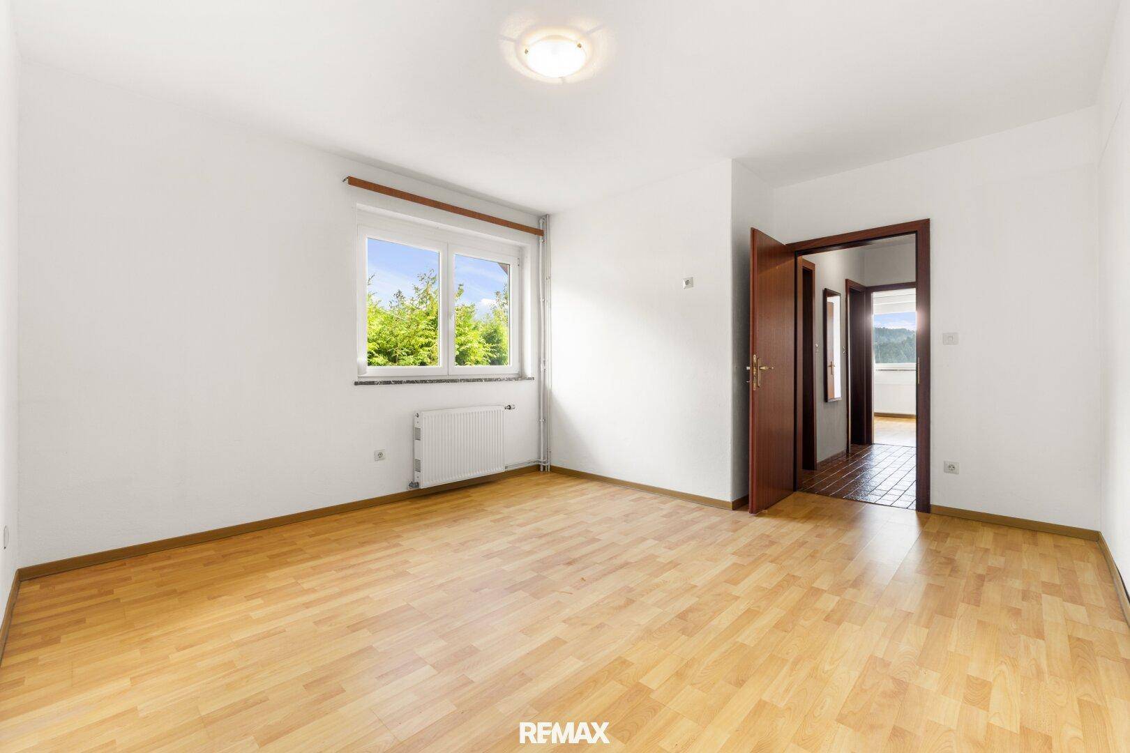 Helles Zimmer mit Parkettboden und Fenster mit Blick ins Grüne.