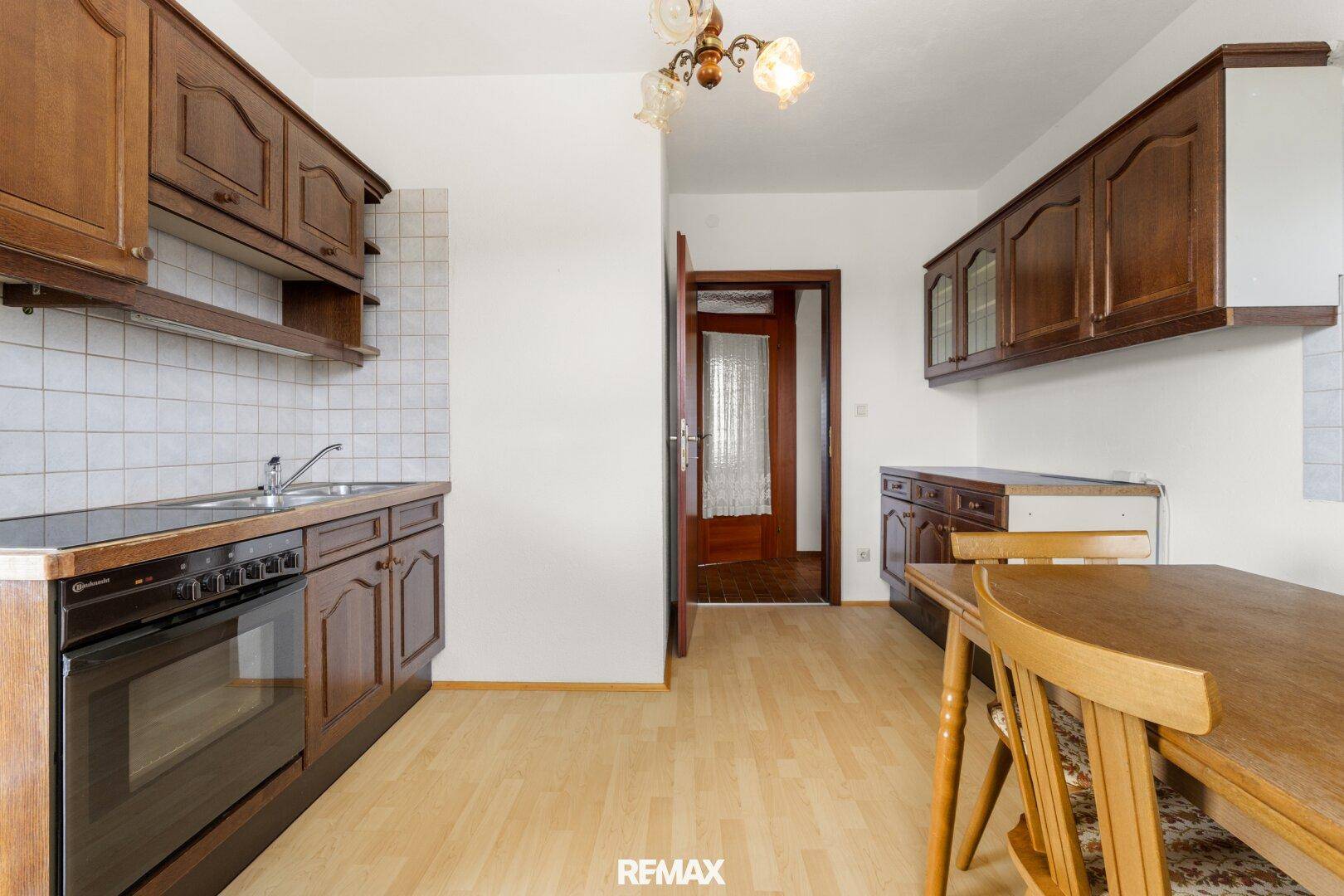 Einfache Küche mit Holzeinbauten, Esstisch und Fenster, bereit zur Modernisierung.