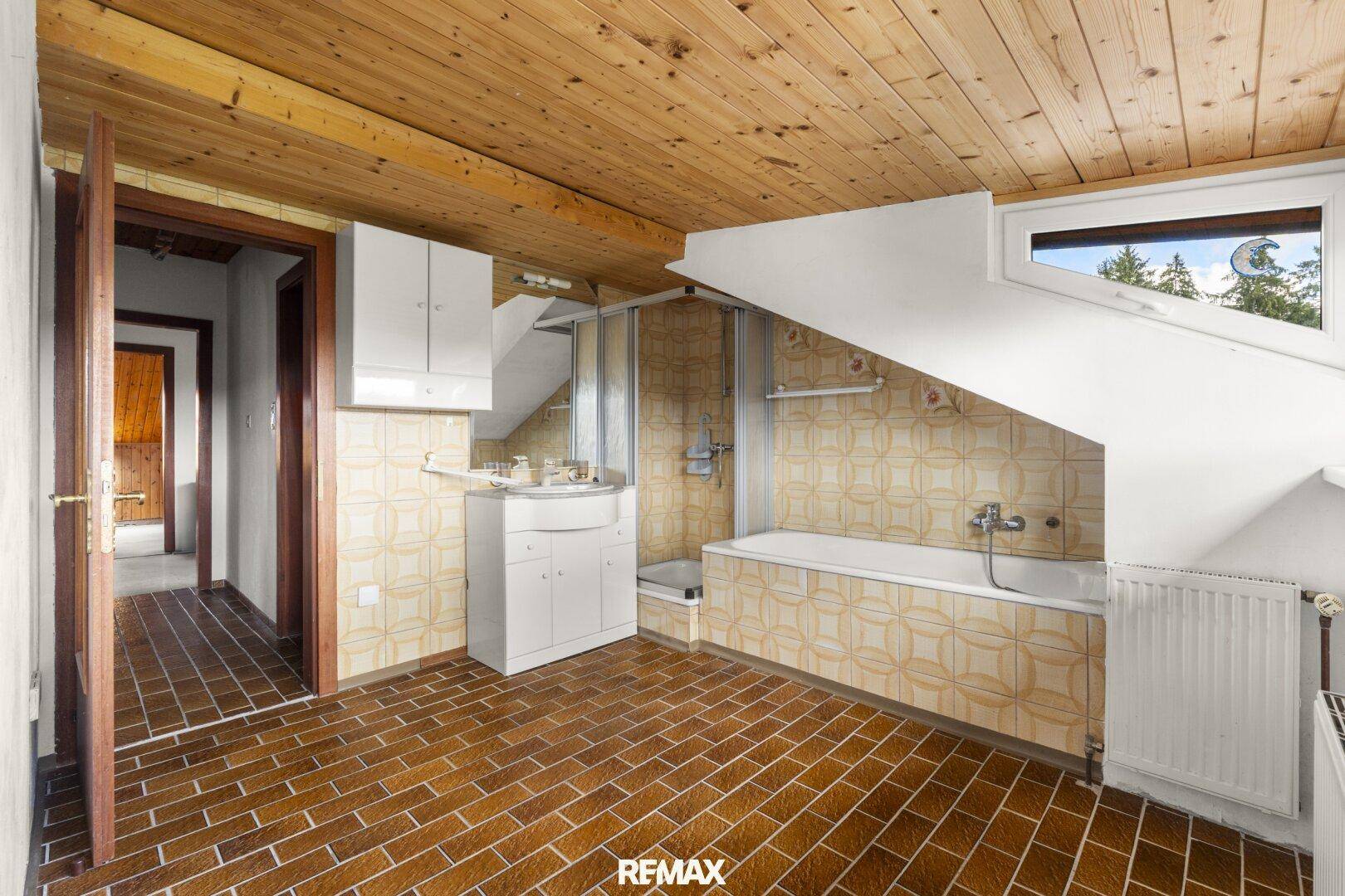Badezimmer im Dachgeschoss mit Badewanne, Dusche und Holzdecke.