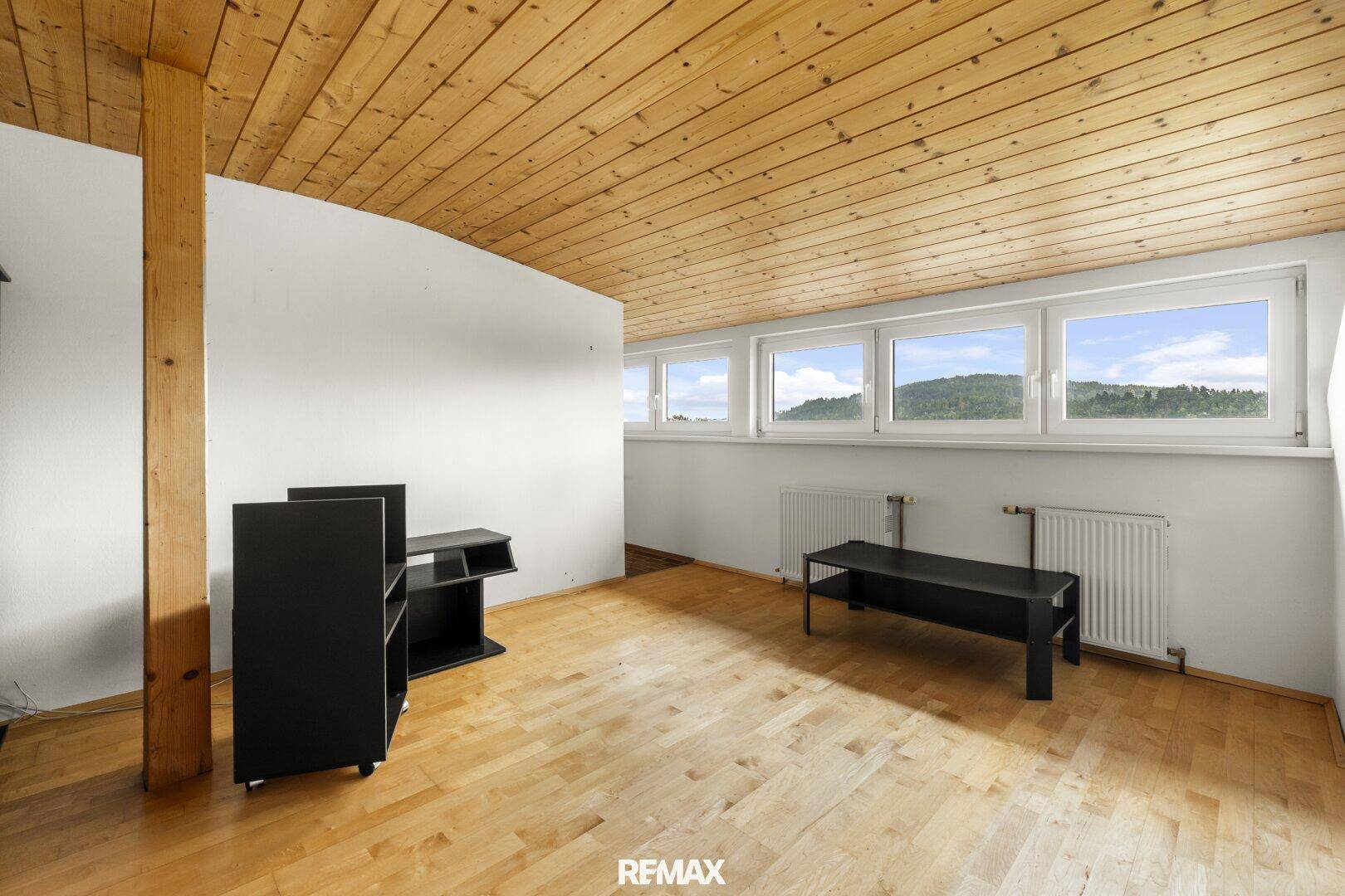 Dachzimmer mit Holzdecke, Parkettboden und mehreren Fenstern für viel Licht.