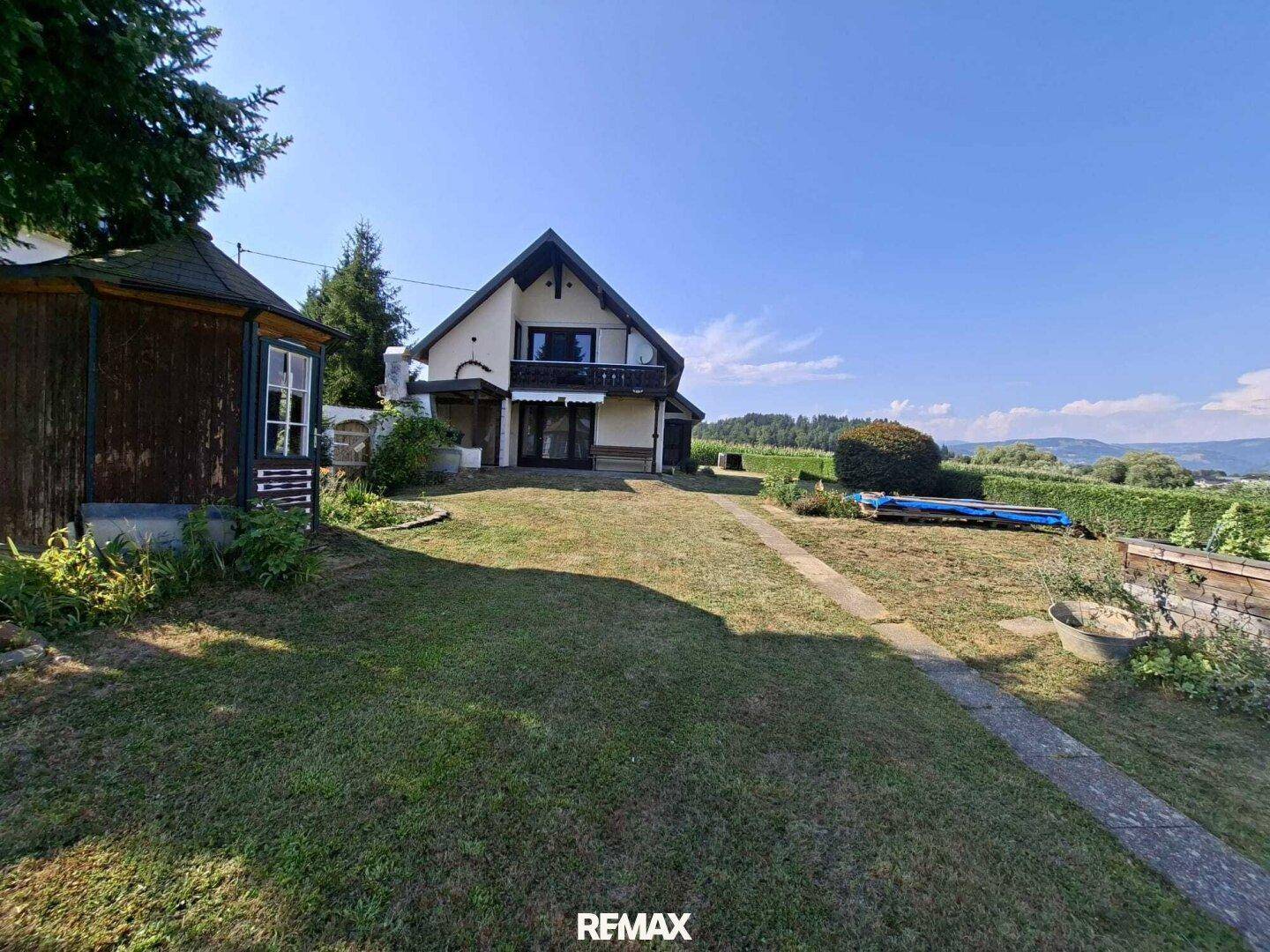 Haus und Garten mit Pavillon und einer blauen Abdeckung, umgeben von grüner Landschaft.