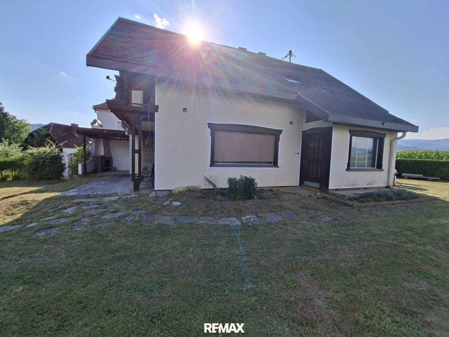 Seitenansicht des Hauses mit überdachtem Bereich und Sonneneinstrahlung, umgeben von Rasen.