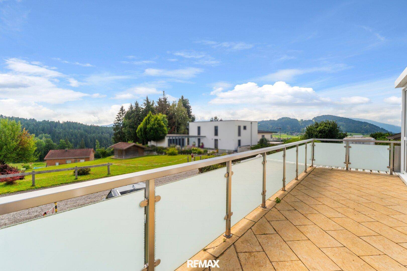 Geräumige Terrasse mit Glasgeländer und weitem Blick auf die umliegende Landschaft.