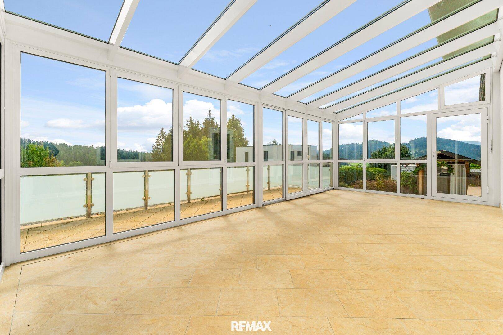 Heller Wintergarten mit großen Glasflächen und Panoramablick auf die grüne Umgebung.