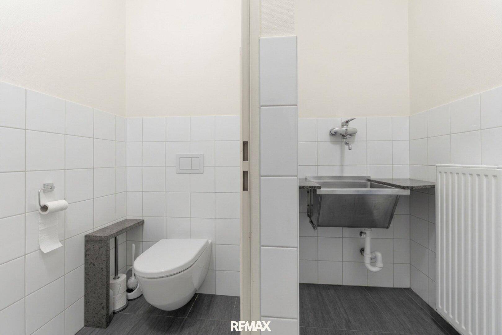 Einfache Toilettenanlage mit WC und Waschbecken, funktional und sauber.