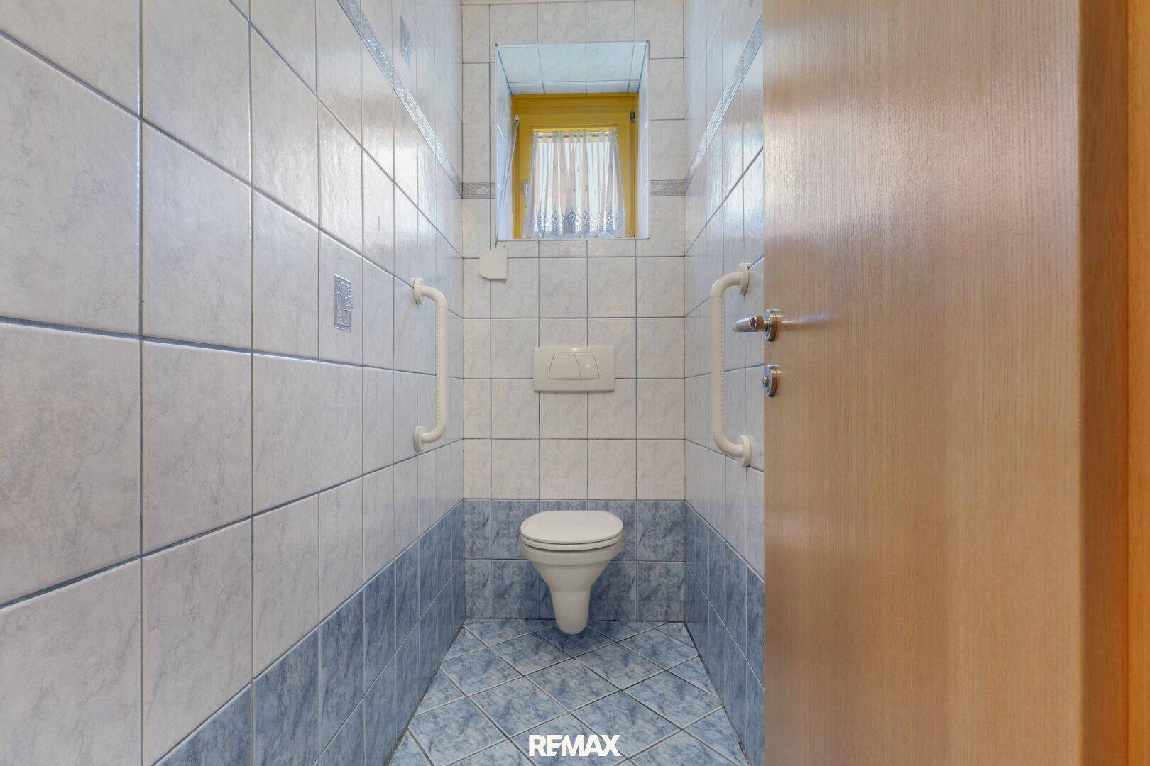 Separate Toilette mit blauen Fliesen und Haltegriffen für mehr Sicherheit.