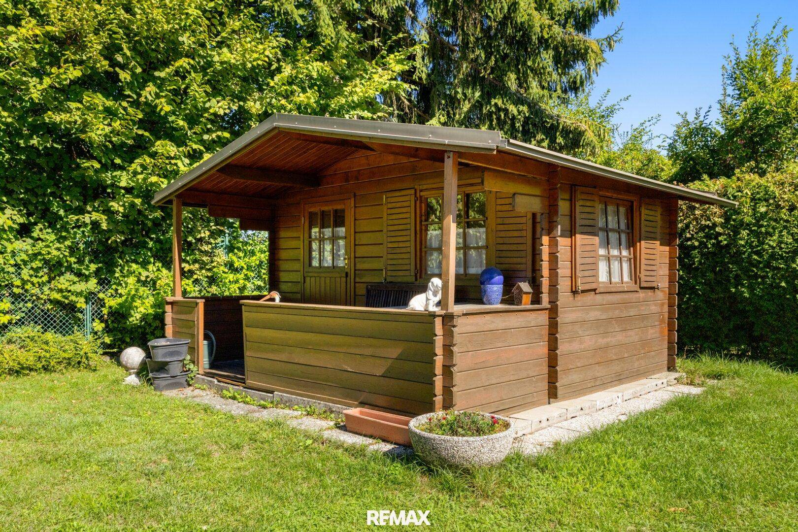Gemütliches Gartenhaus aus Holz, umgeben von Grünflächen und Bäumen.