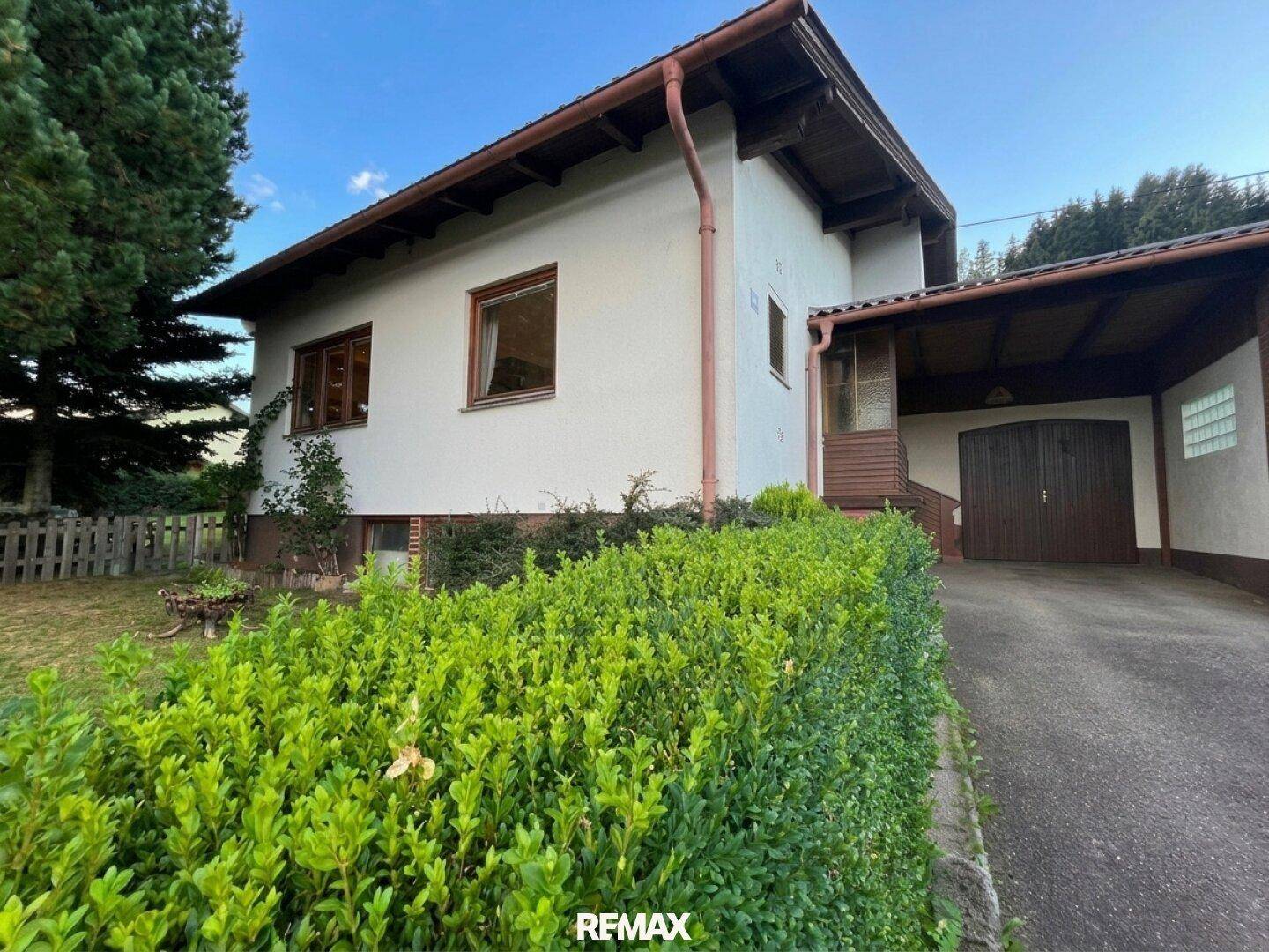 Einfamilienhaus mit Carport, gepflegter Hecke und Zufahrt auf einem sonnigen Grundstück am Abend.