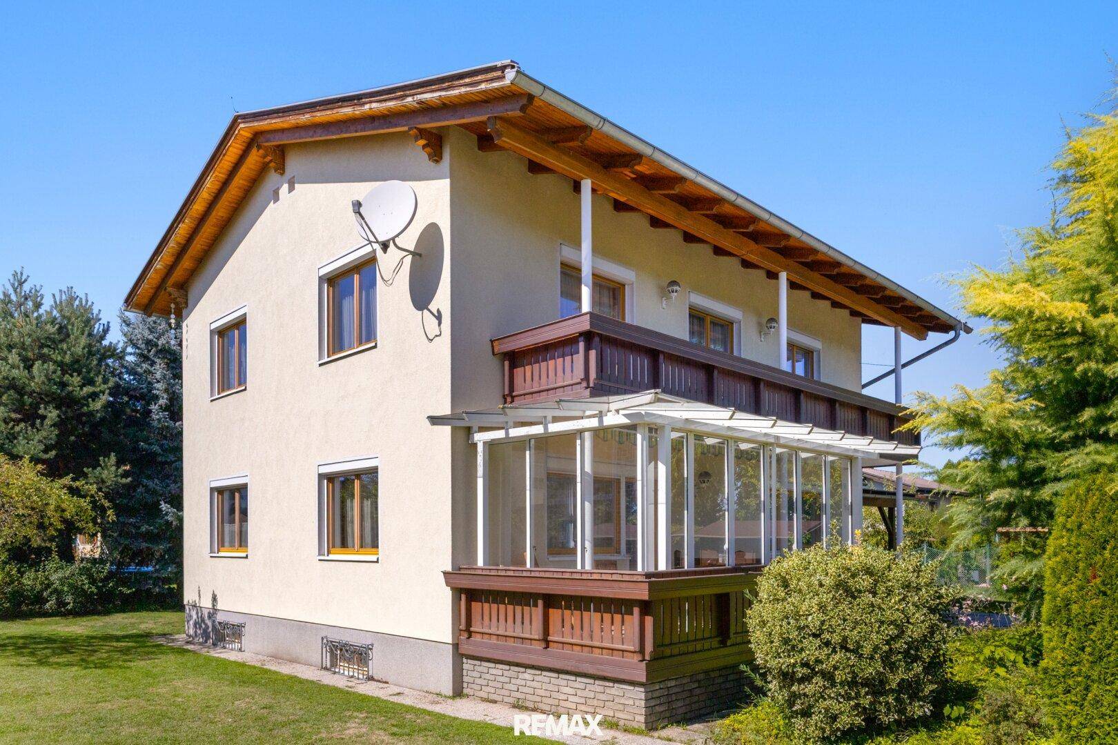 Seitenansicht des Hauses mit Wintergarten und Balkon, umgeben von viel Grün.