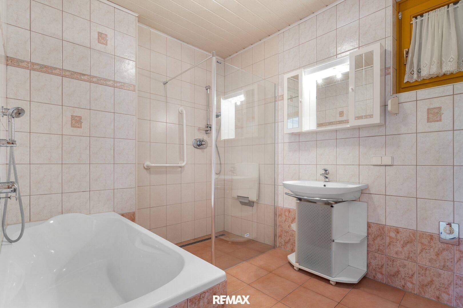 Badezimmer mit Badewanne, Dusche und beigefarbenen Fliesen, barrierefrei ausgestattet.