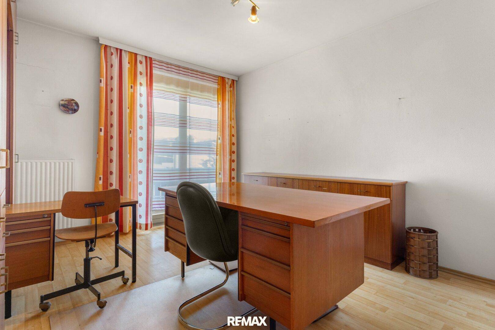 Arbeitszimmer mit Holzboden, Schreibtisch und bunten Vorhängen.