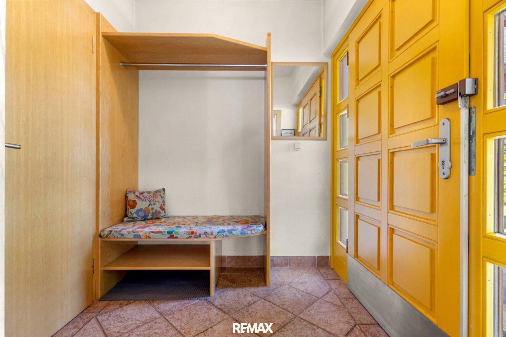 Eingangsbereich mit Garderobe, Fliesenboden und gelber Eingangstür.