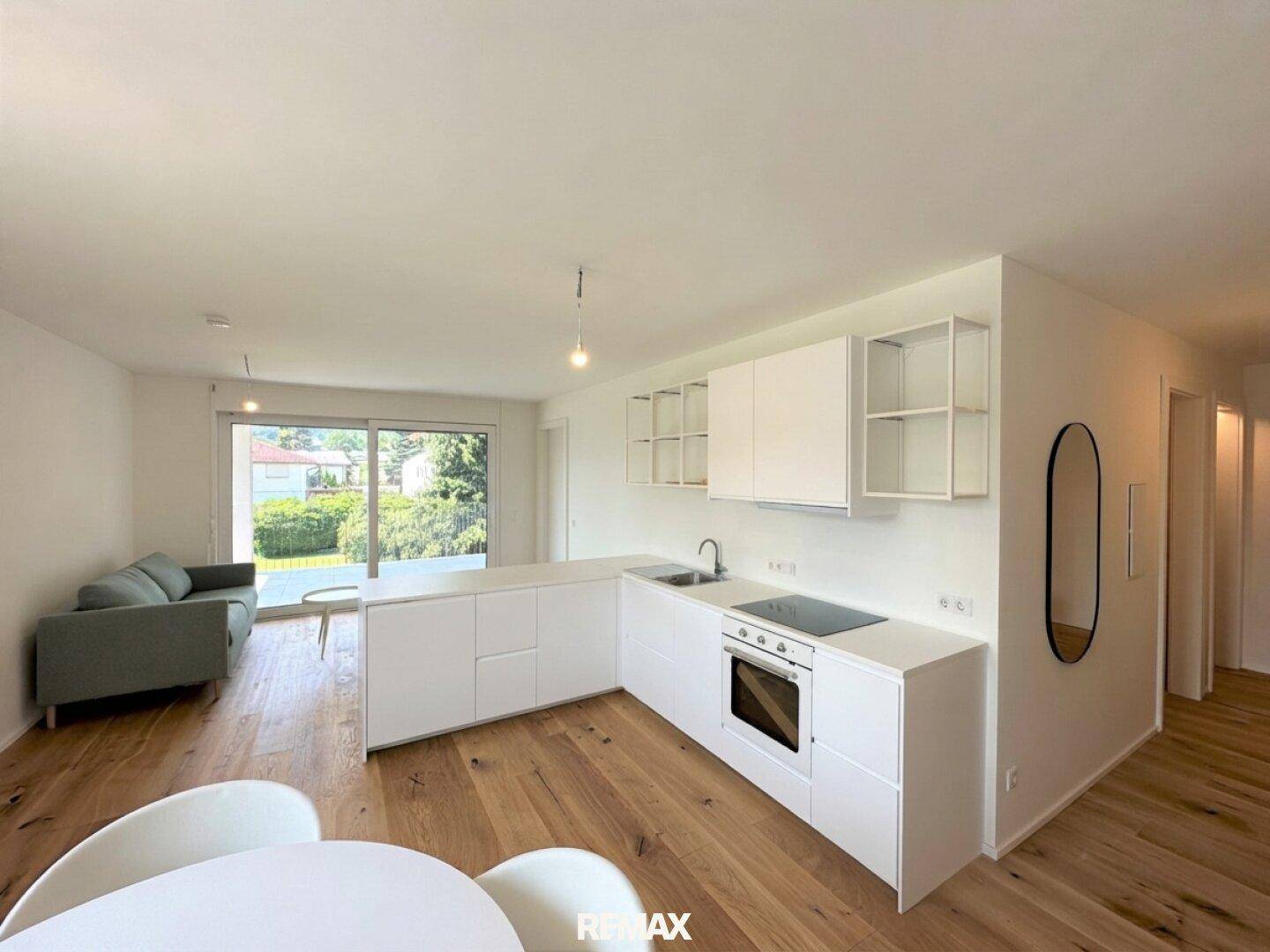 Heller offener Wohn-Essbereich mit moderner weißer Küche, Holzboden und Zugang zur Terrasse.