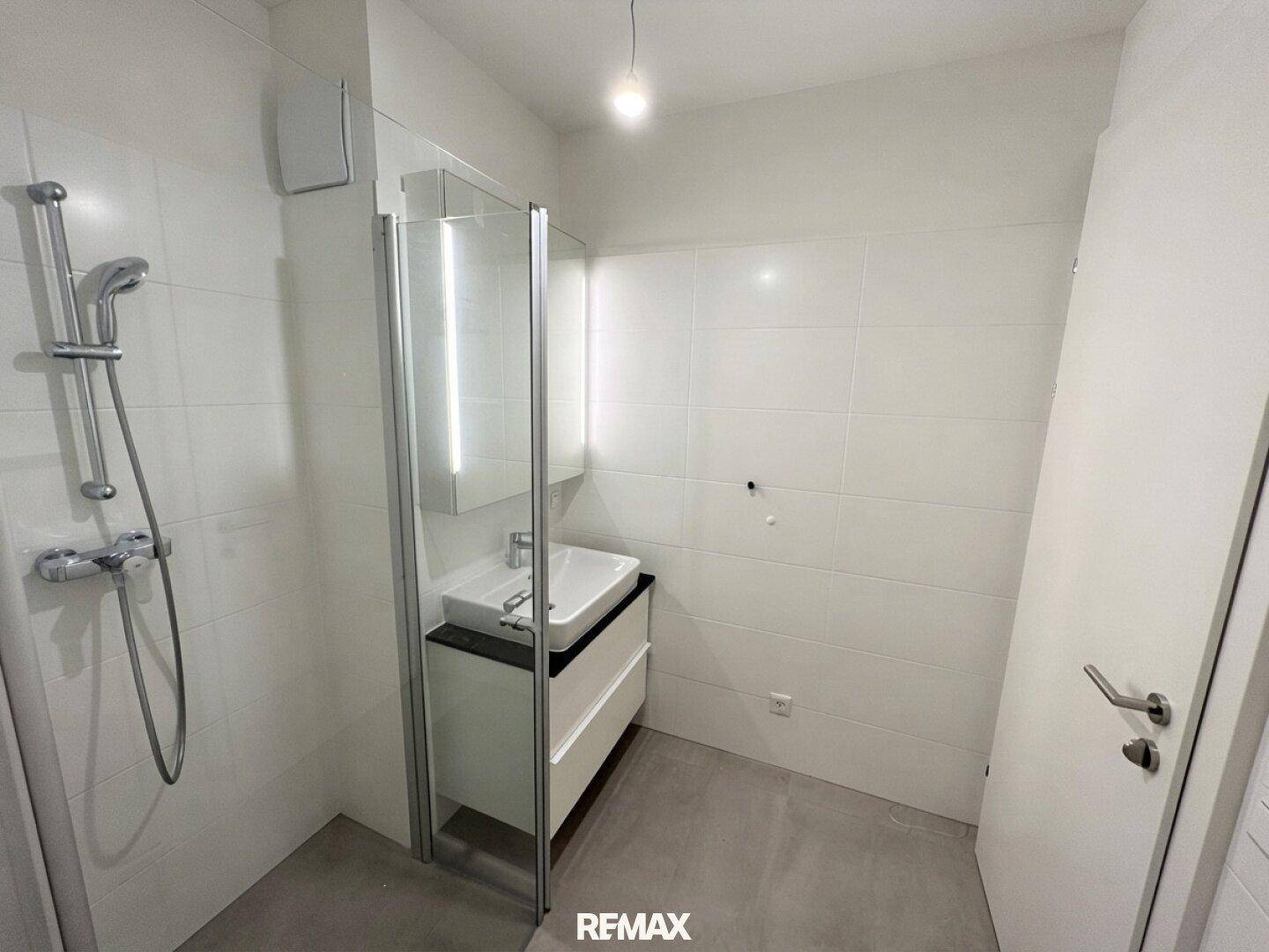 Modernes Badezimmer mit weißen Fliesen, Duschbereich und elegantem Einzelwaschbecken.