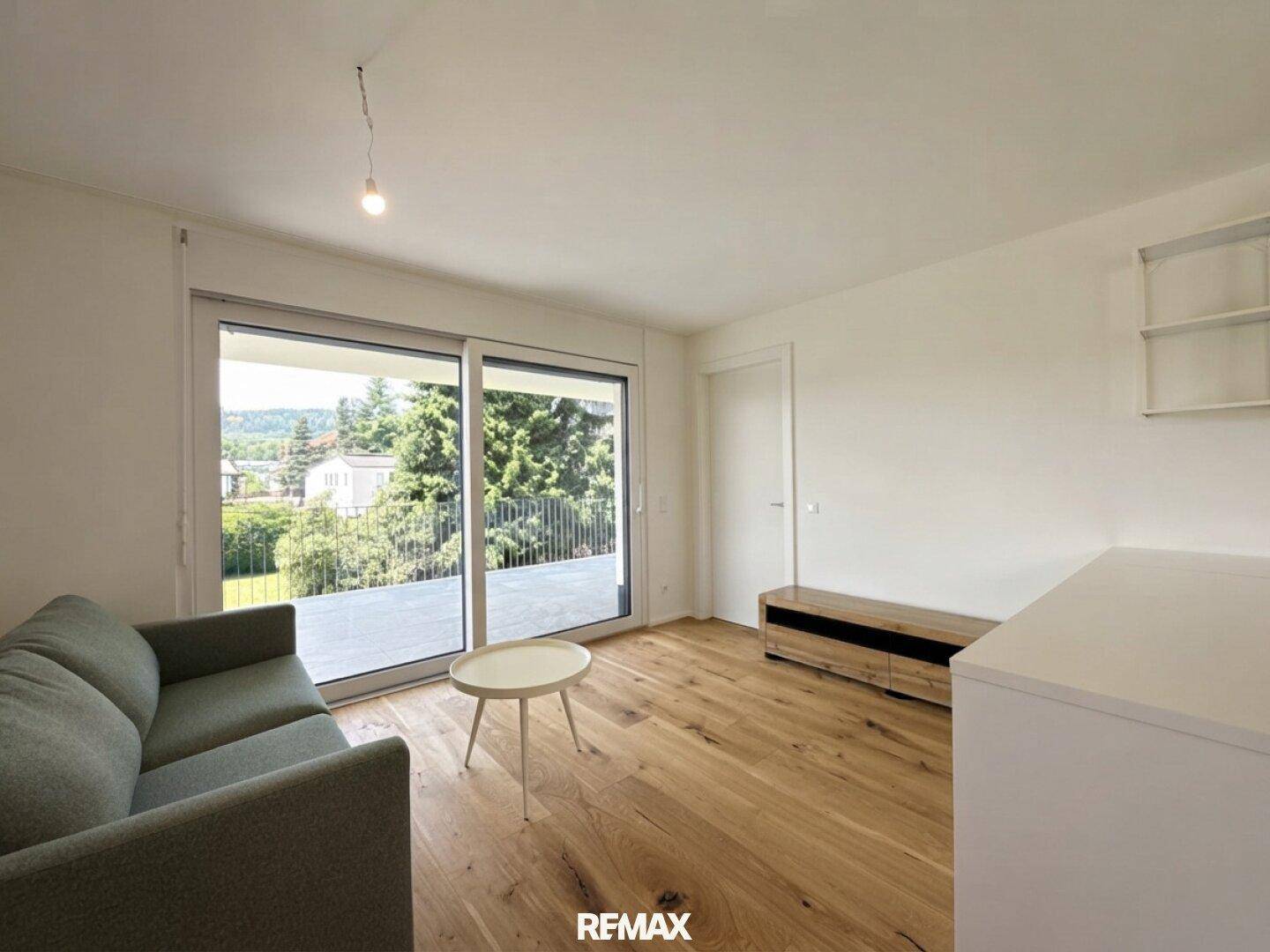 Gemütliches Wohnzimmer mit Holzboden, Sofa und großer Schiebetür zur Außenterrasse.