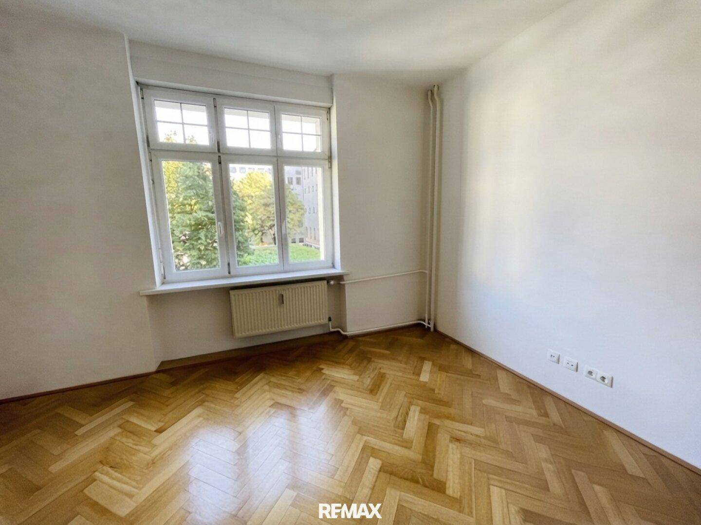 Lichtdurchfluteter Raum mit elegantem Fischgrätparkett und Blick auf die grüne Umgebung.