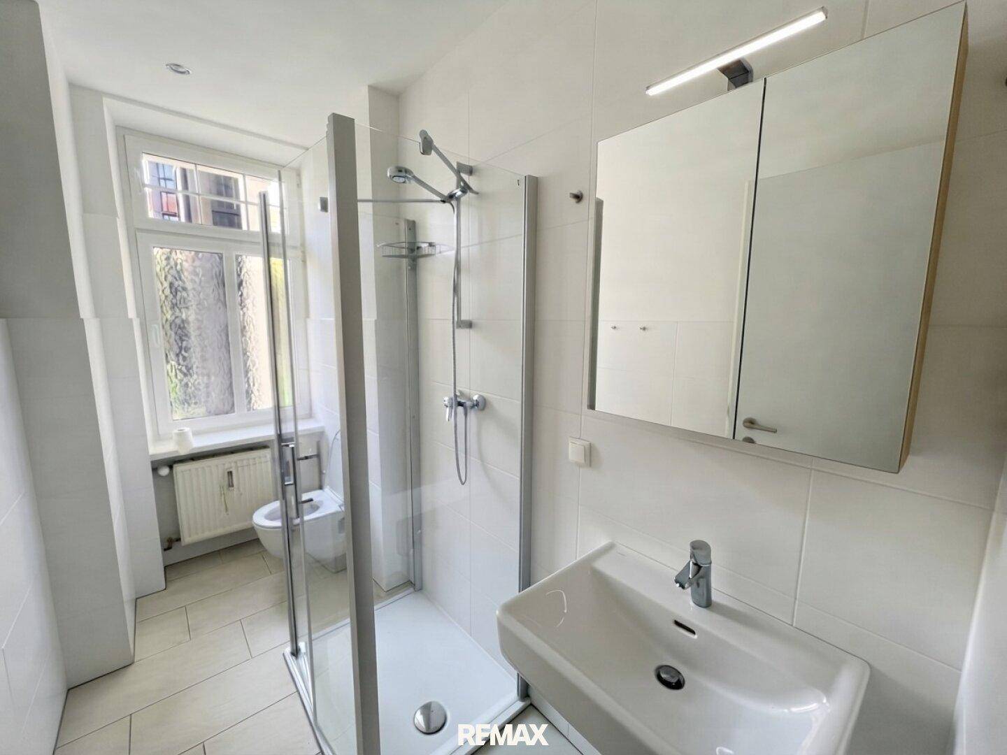 Modernes Badezimmer mit weiß gefliesten Wänden, Duschkabine und Fenster für Tageslicht.