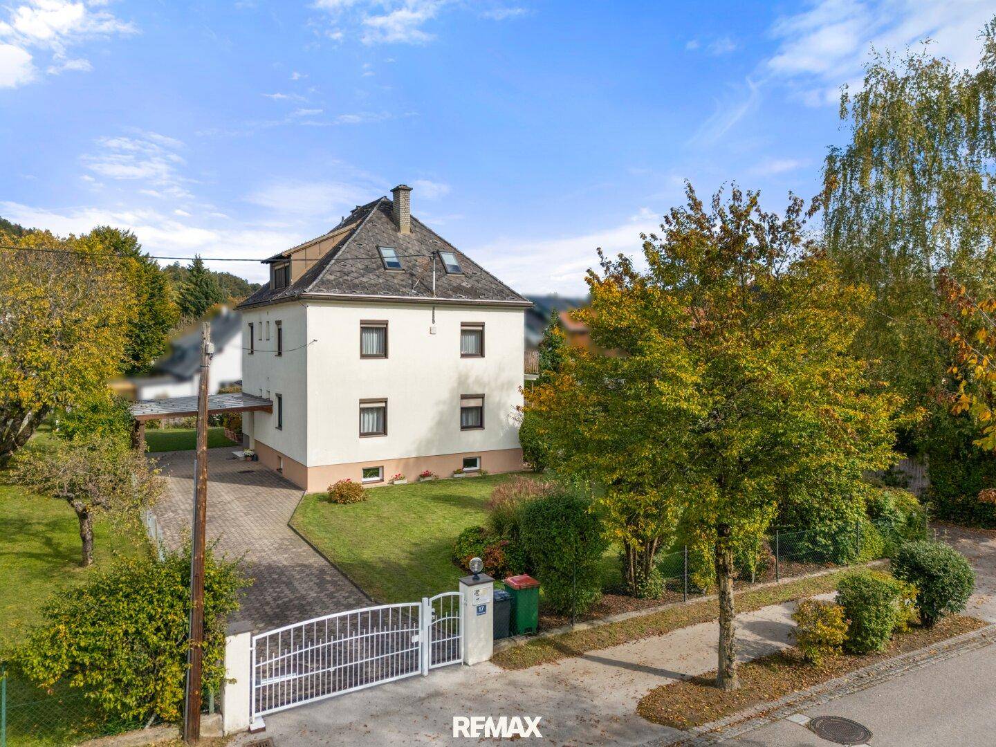 Ansicht des Hauses von der Straße mit Einfahrt, Vorgarten und geschlossenem Tor.