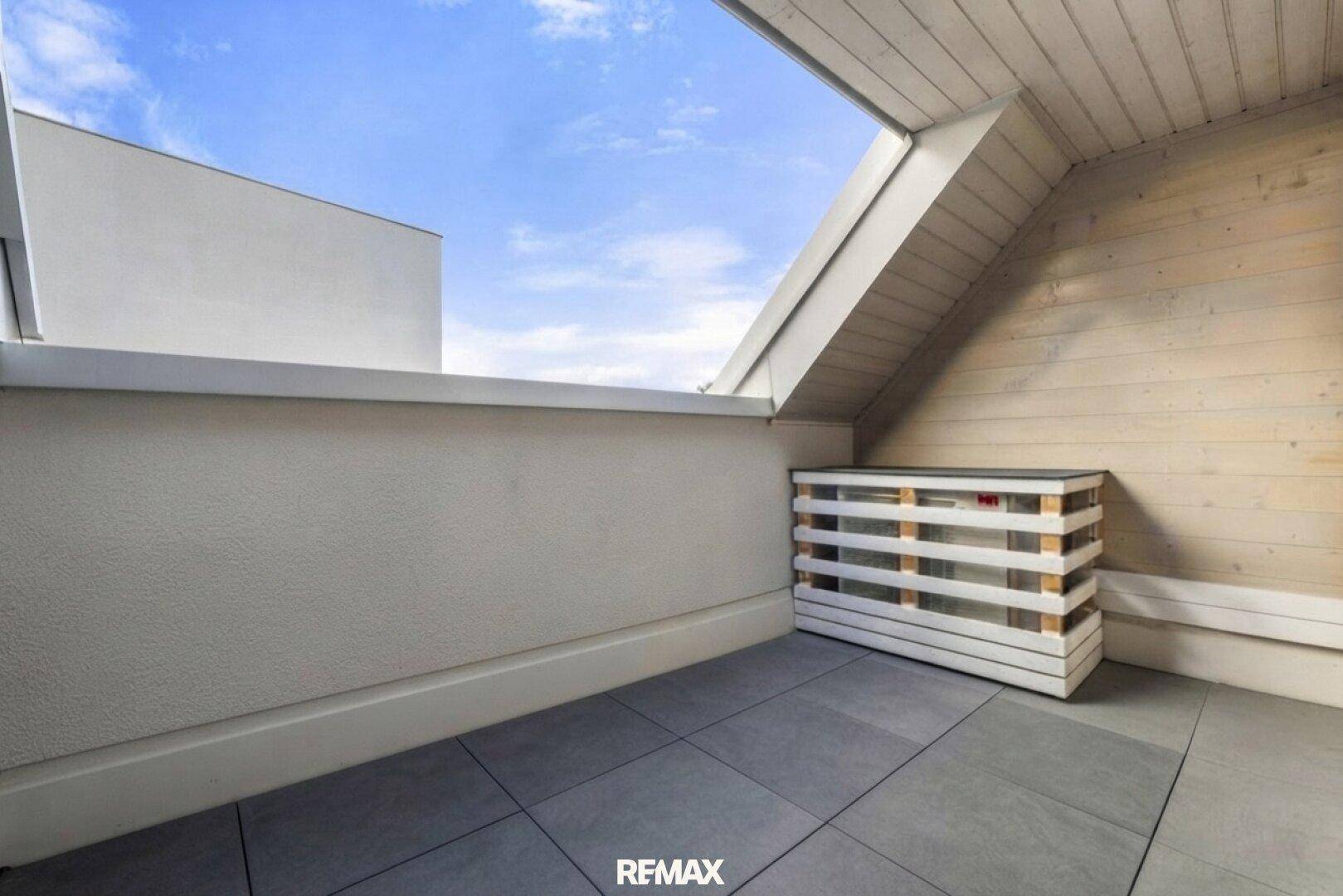 Kleine, geflieste Dachterrasse mit Holzdachschräge und Blick in den Himmel, ideal für entspannte Stunden.