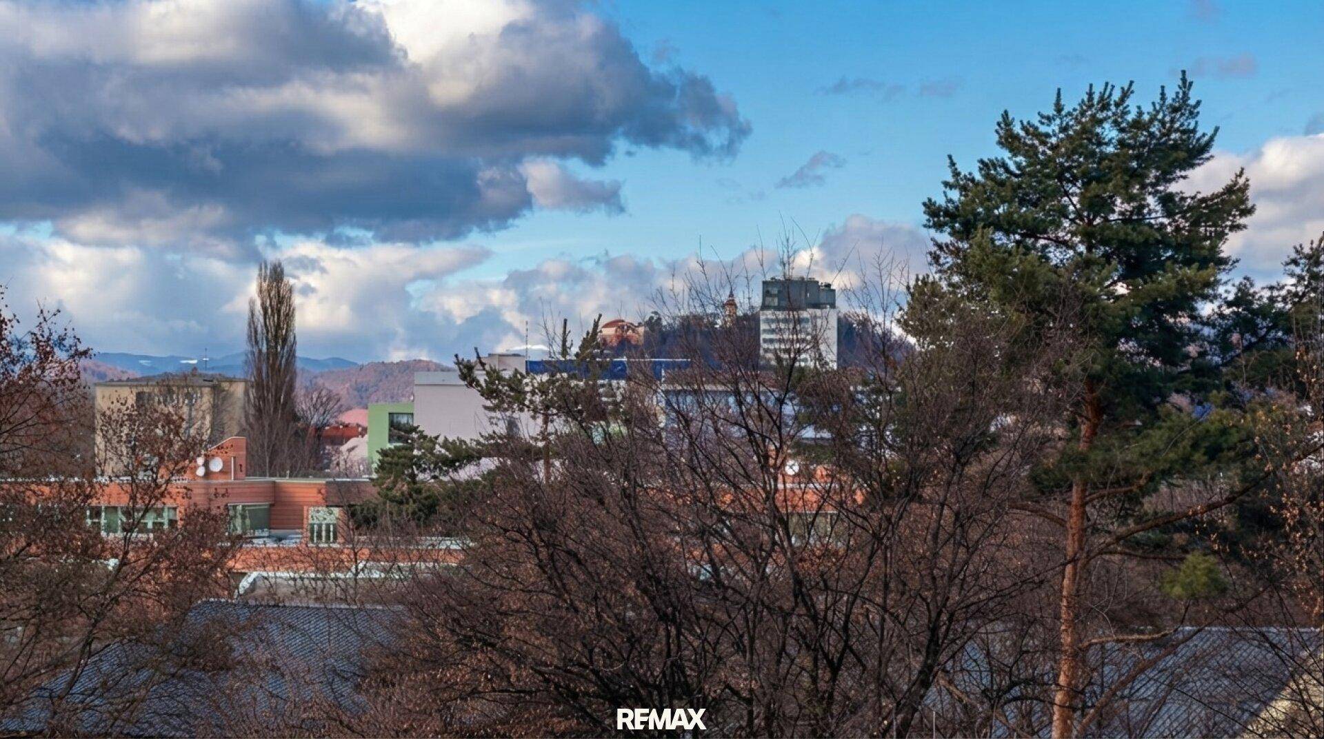 Panoramablick über die Stadt mit bewölktem Himmel und Bäumen im Vordergrund.