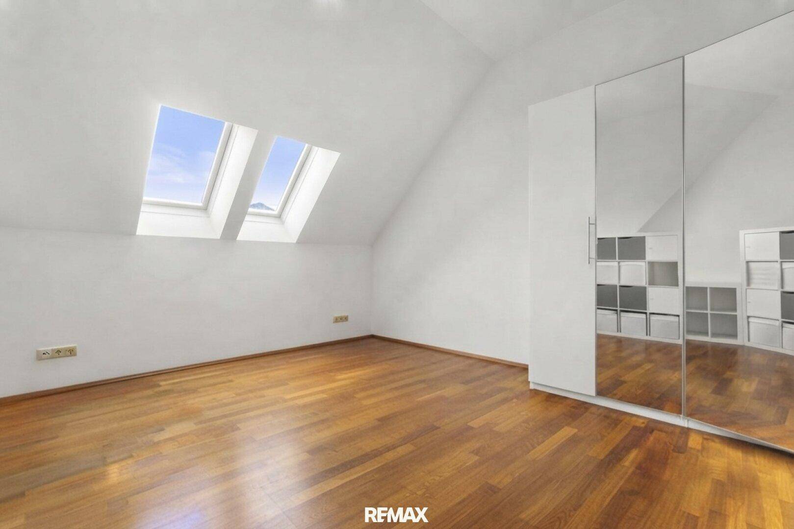 Helles Schlafzimmer mit Holzfußboden, Dachschrägen und einem großen Spiegelschrank, der den Raum erweitert.