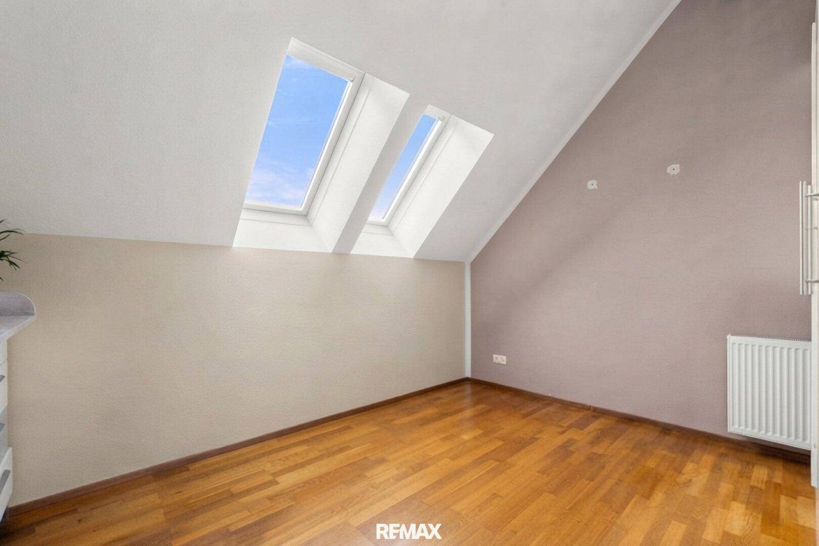 Gemütliches Zimmer mit Holzboden, Dachschrägen und zwei Dachfenstern, die für eine angenehme Helligkeit sorgen.