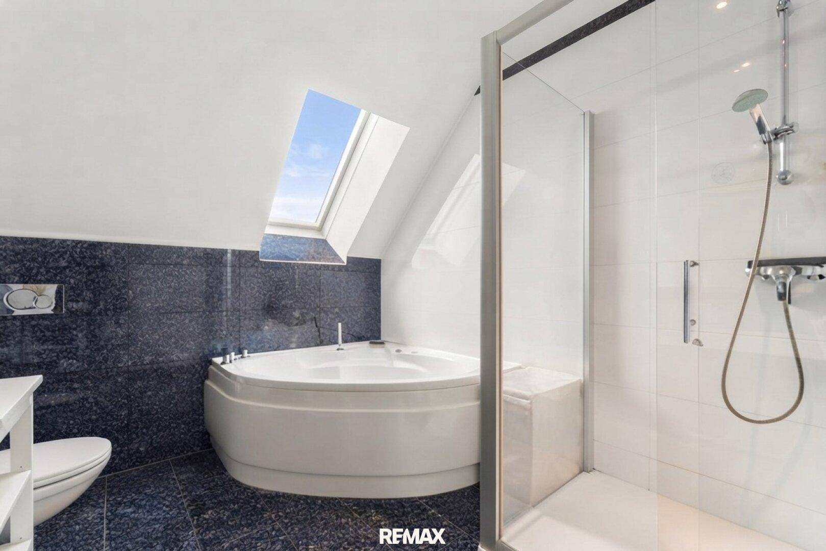 Geräumiges Badezimmer mit Eckbadewanne, separater Dusche und einem Dachfenster, das den Raum erhellt.