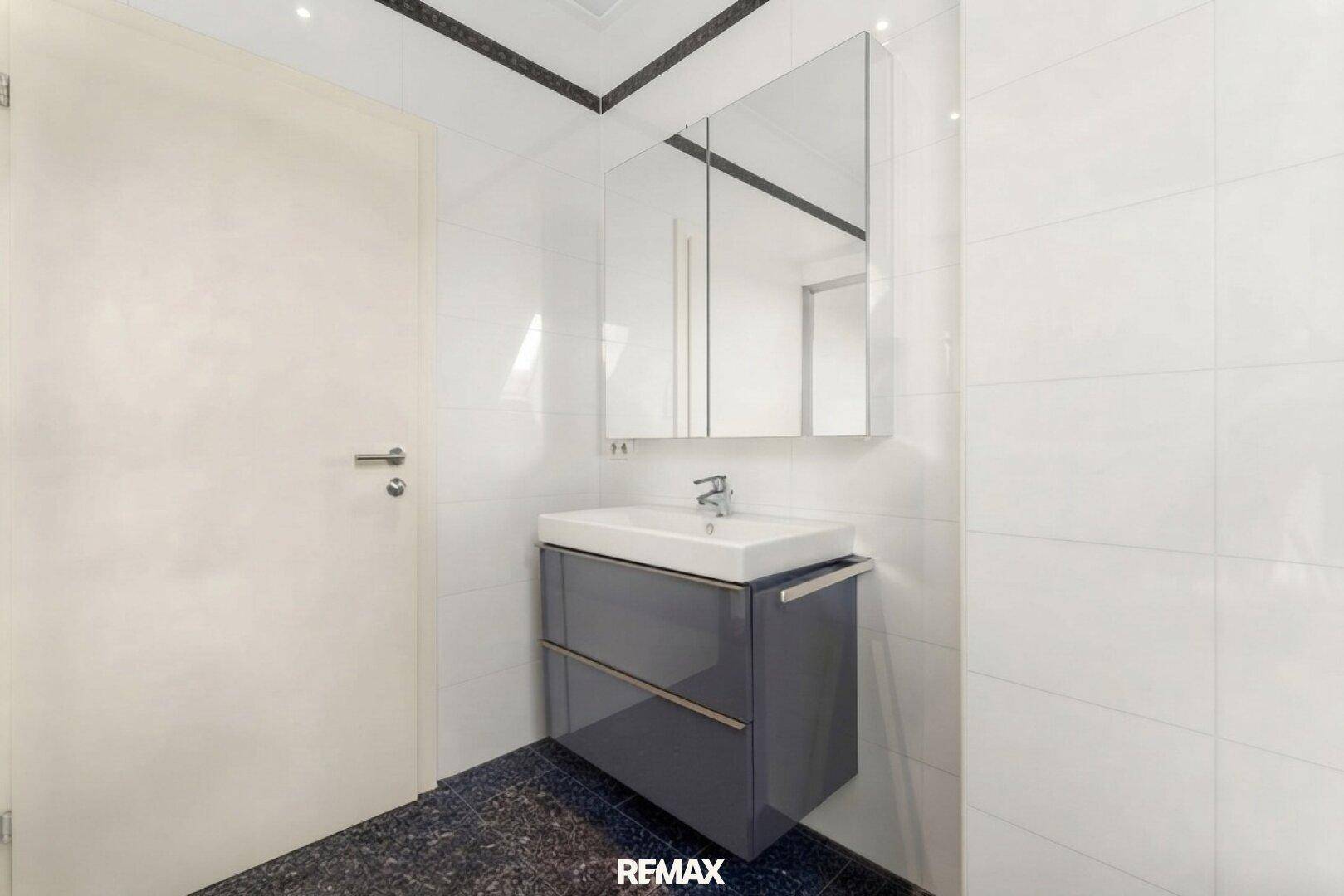 Modernes Badezimmer mit weißem Fliesen, dunklem Boden und einem stilvollen Waschtisch mit Spiegelschrank.
