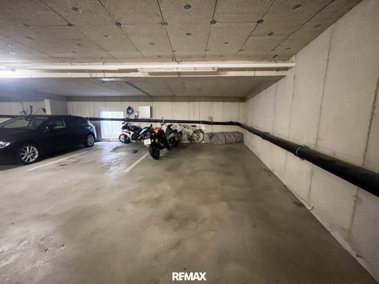 Tiefgarage mit Betonwänden und -decke, bietet Stellplätze für Autos und Motorräder.