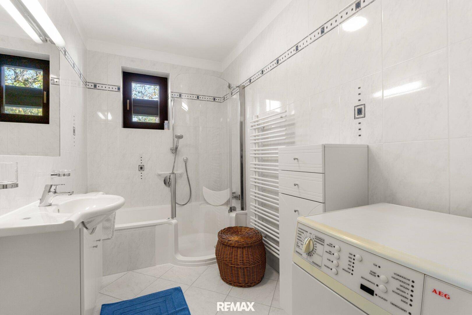 Helles Badezimmer mit Badewanne, Dusche, Waschbecken und Waschmaschine, komplett gefliest.