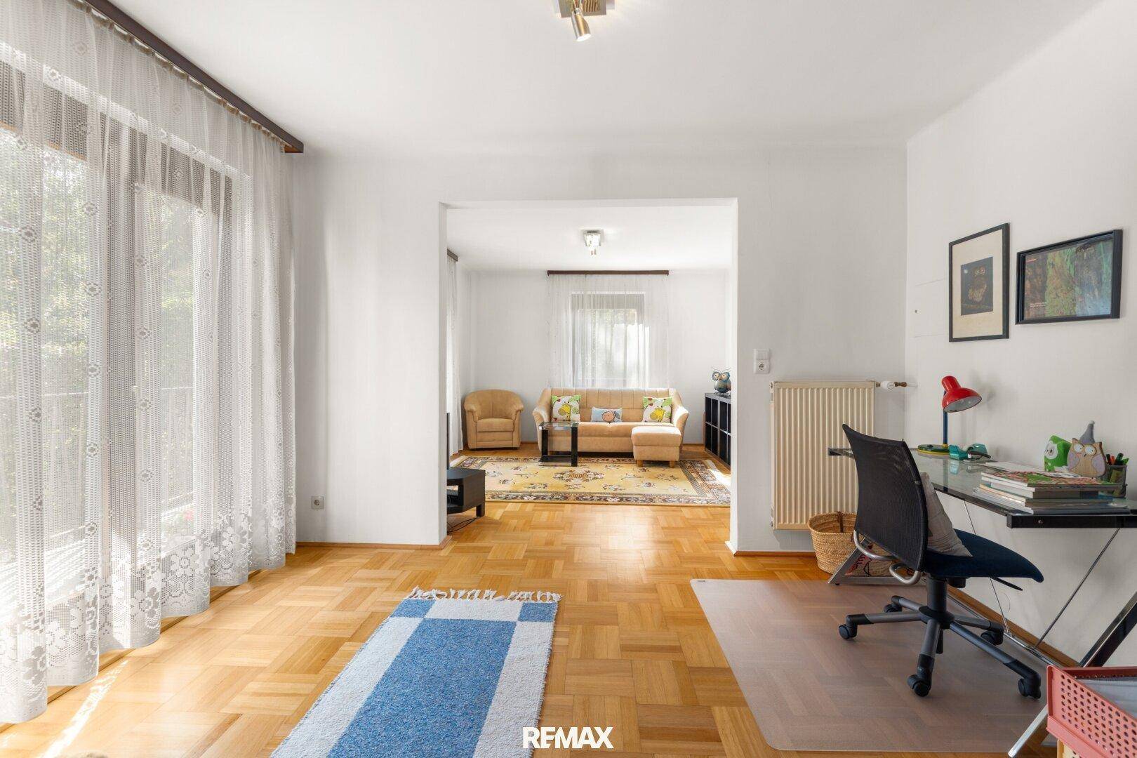 Heller Raum mit Schreibtisch und Zugang zu einem weiteren Wohnbereich, ideal als Büro.