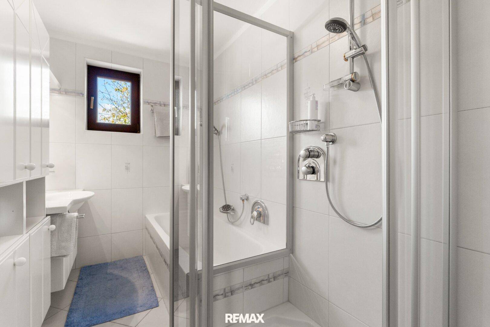 Modernes Badezimmer mit Duschkabine, Badewanne, Waschbecken und Fenster, hell gefliest.