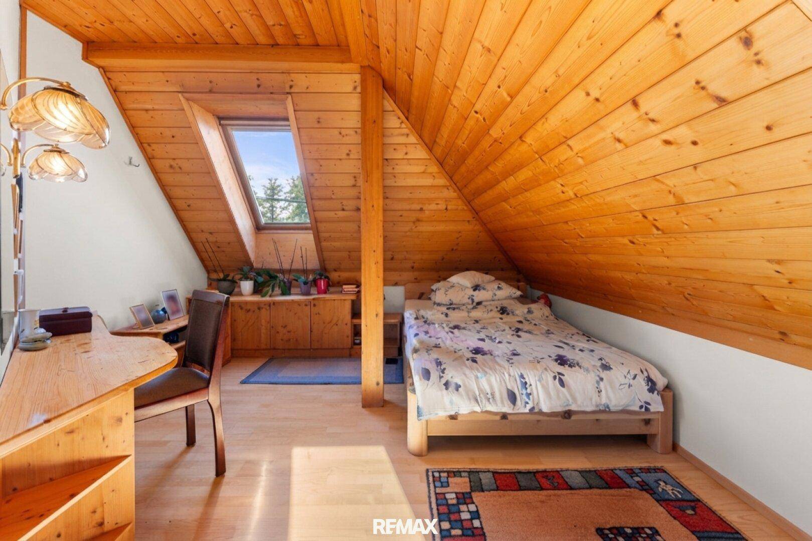 Gemütliches Schlafzimmer im Dachgeschoss mit Holzverkleidung, Dachfenster und Einzelbett.