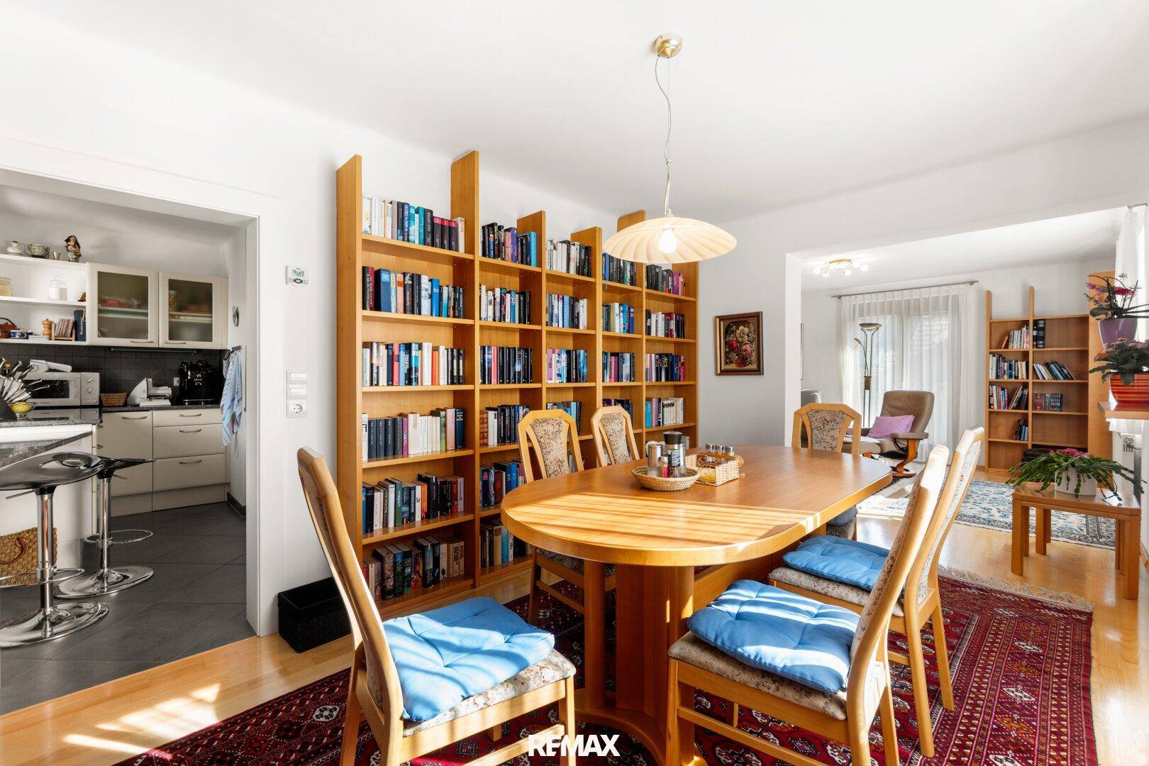 Gemütlicher Essbereich mit großem Holztisch, Bücherregalen und Zugang zur Küche.