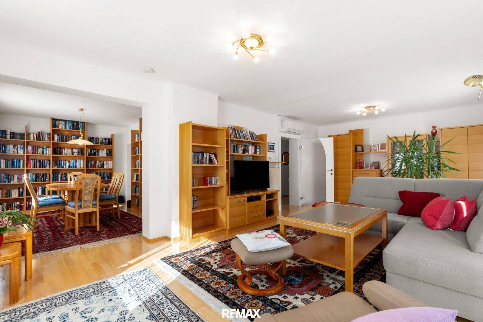 Helles Wohnzimmer mit Sofa, TV-Möbeln und Blick auf den Essbereich mit Bücherregalen.