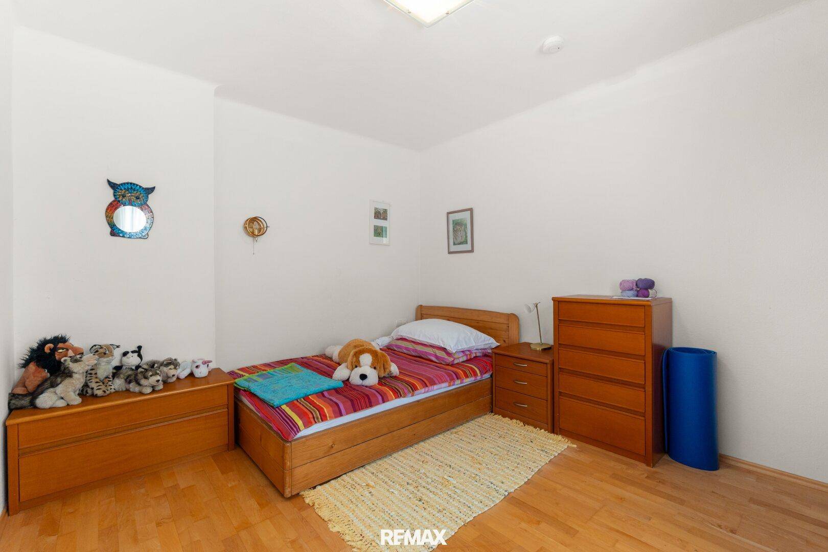 Kinderzimmer mit Einzelbett, Holzmöbeln und Spielzeug, bietet eine gemütliche Atmosphäre.