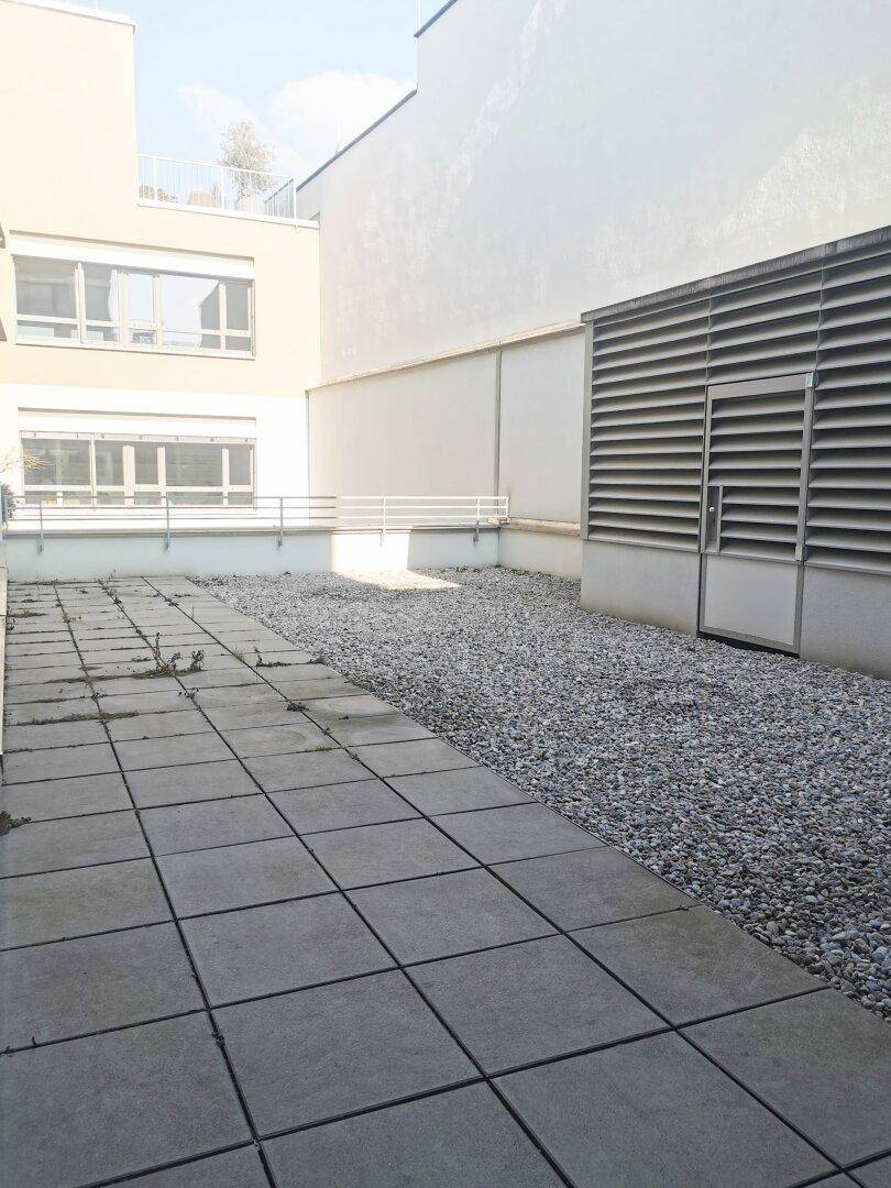 Außenbereich mit Betonplatten und Kiesfläche neben einem modernen Gebäude.