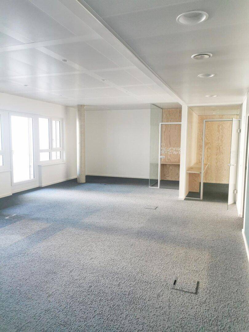 Großzügiger, leerer Bürobereich mit Teppichboden, vielen Fenstern und modernen Trennwänden.